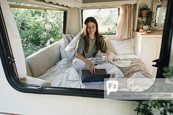 Junge Freiberuflerin mit Laptop auf dem Bett im Wohnmobil