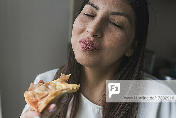 Frau mit geschlossenen Augen isst Pizza zu Hause