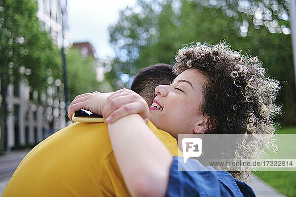 Glückliche junge Frau mit geschlossenen Augen  die ihren Freund im Park umarmt