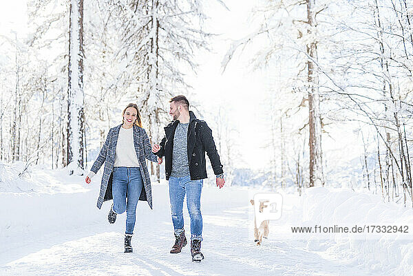 Young couple walking with dog in snow during vacation