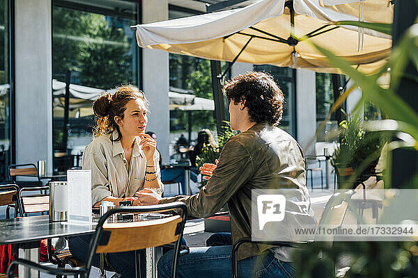 Couple talking while siting at sidewalk cafe on sunny day