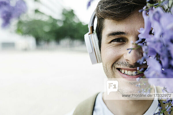 Lächelnder Mann mit Kopfhörern hinter lila Blumen