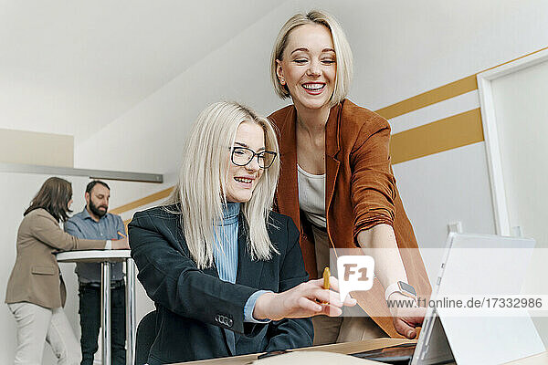 Happy mature businesswoman explaining to female colleague while discussing over digital tablet in office