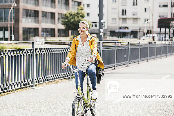 Weibliche Fachkraft lächelt beim Fahrradfahren auf einer Brücke