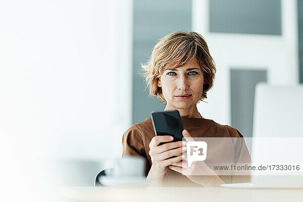 Geschäftsfrau mit Mobiltelefon und Laptop im Büro