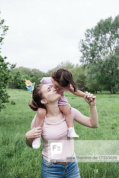 Mutter trägt Tochter auf den Schultern und küsst sie im Park