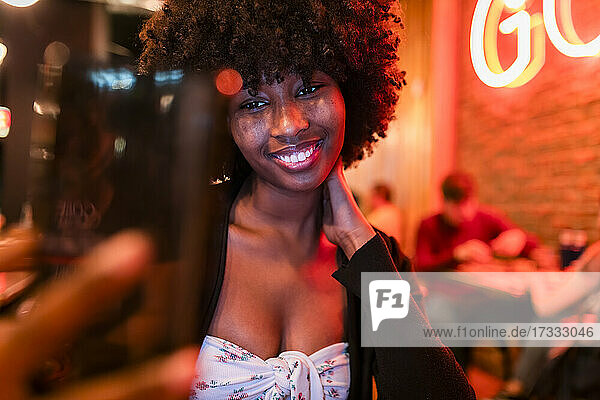 Lächelnde Afro-Frau  die ein Selfie mit ihrem Handy in einer Bar macht