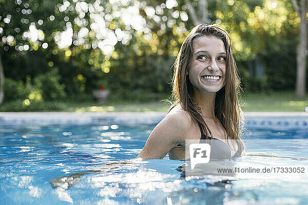 Lächelnde Frau mit braunem Haar im Schwimmbad schaut weg