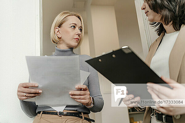 Mature blond businesswoman looking at female professional discussing in office