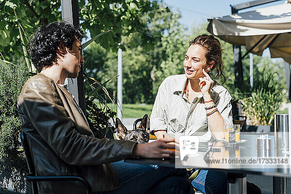Lächelnde Freundin im Gespräch mit ihrem Freund  während sie in einem Straßencafé sitzt