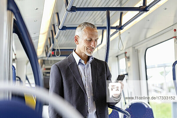 Männlicher Geschäftsmann  der ein Smartphone benutzt  während er in der Straßenbahn steht
