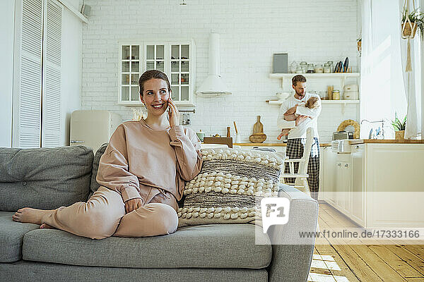 Lächelnde Frau  die mit einem Smartphone spricht  während der Mann seine Tochter zu Hause trägt