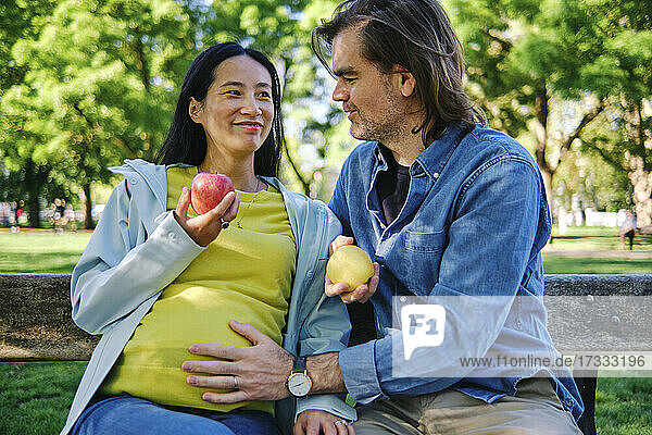 Pflegender Ehemann mit Hand auf dem Bauch seiner Frau  während er in einem öffentlichen Park sitzt