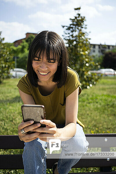 Lächelnde Frau  die ein Smartphone benutzt  während sie auf einer Bank sitzt