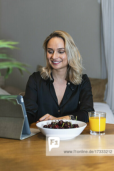 Young businesswoman working on digital tablet with bowl of cherries and juice at desk in home office
