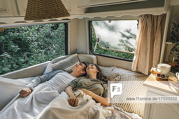 Lächelndes junges Paar liegt zusammen auf einem Bett im Wohnmobil