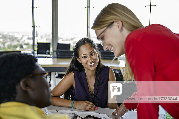 Lächelnde Geschäftsfrauen  die einen männlichen Kollegen ansehen  während sie bei einer Besprechung im Büro diskutieren