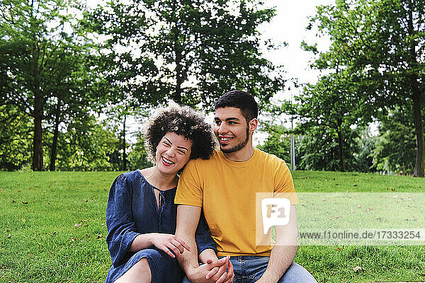 Happy young couple holding hands while sitting together at park