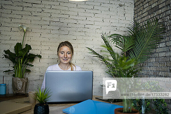 Lächelnde junge Berufstätige mit Laptop am Tisch im Home Office