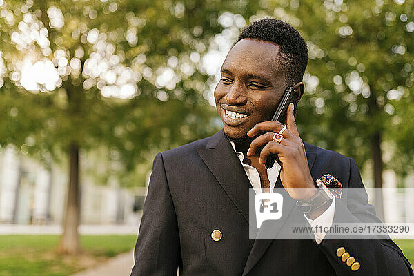 Lächelnder junger Mann  der im Park mit seinem Smartphone telefoniert