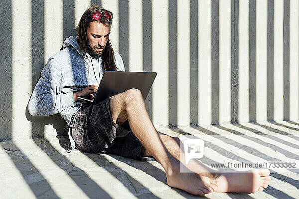 Junger männlicher Freiberufler mit Laptop an einem sonnigen Tag