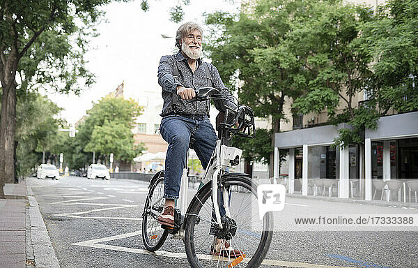 Glücklicher reifer Mann mit Elektrofahrrad auf der Straße in der Stadt