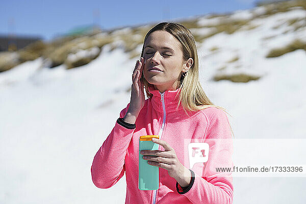 Woman with eyes closed applying sunscreen on face during sunny day