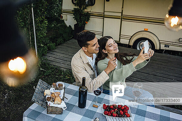 Lächelnde junge Frau  die ein Selfie mit ihrem Freund macht  während sie am Tisch sitzt