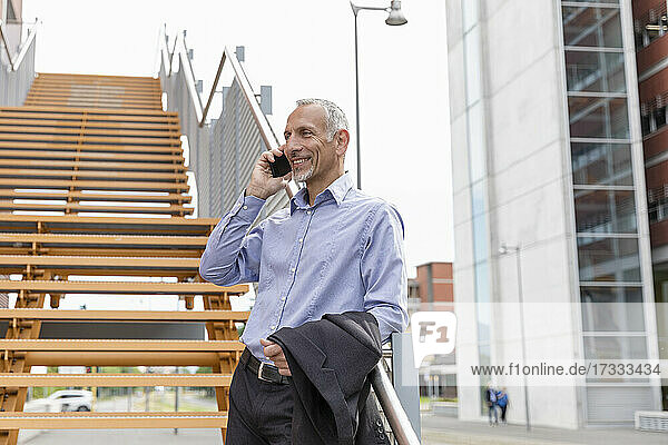 Geschäftsmann  der mit seinem Smartphone spricht  während er sich am Geländer einer Treppe abstützt