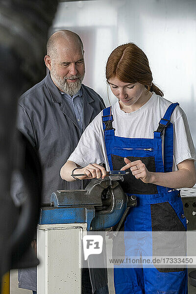 Weiblicher Auszubildender bei der Arbeit mit Maschinen  während ein männlicher Ausbilder in der Werkstatt assistiert