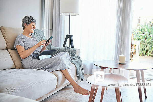 Frau  die ihr Smartphone benutzt  während sie auf dem Sofa im heimischen Wohnzimmer sitzt