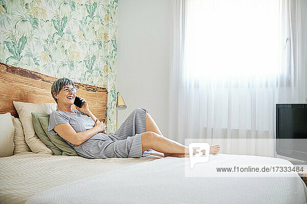 Reife Frau  die mit ihrem Smartphone spricht  während sie im Schlafzimmer zu Hause sitzt