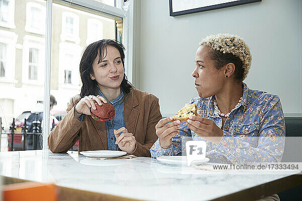 Lesbian couple eating fast food while sitting at table in cafe