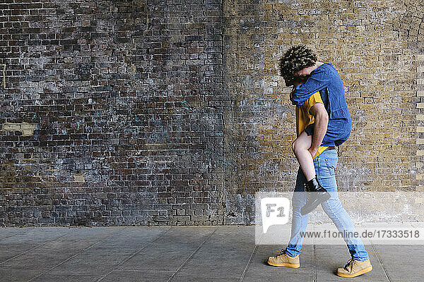 Junger Mann nimmt seine Freundin auf dem Gehweg an der Mauer huckepack