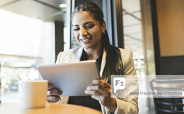 Geschäftsfrau lächelt bei der Nutzung eines digitalen Tablets in einem Café