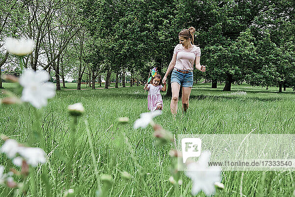 Mädchen hält Windrädchen beim Spaziergang mit Mutter im Park