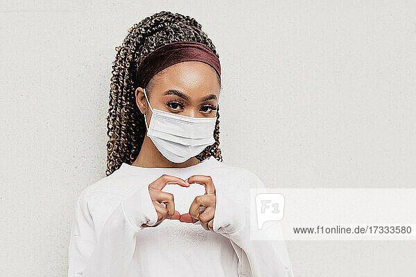 Young woman wearing protective face mask making heart shape from hands