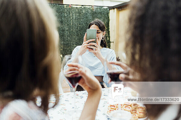 Frau  die ihre Freunde mit dem Smartphone fotografiert  während sie am Tisch sitzt