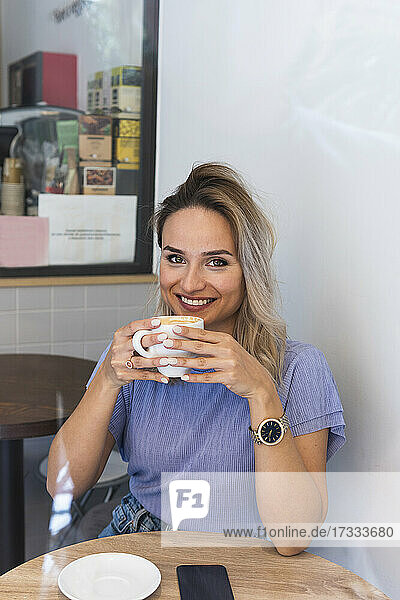 Lächelnde junge Frau trinkt Kaffee in einem Cafe
