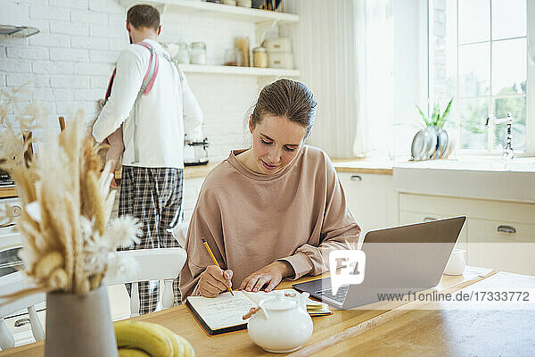 Geschäftsfrau schreibt in Tagebuch mit Mann und Tochter in Küche zu Hause