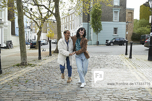 Happy lesbian couple laughing while walking together on footpath