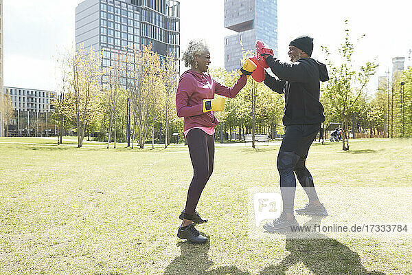 Smiling woman wearing gloves practicing boxing with man at park