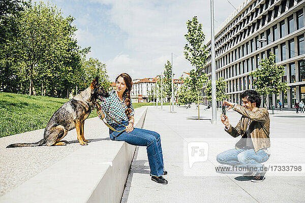 Mann fotografiert Frau mit Hund in der Stadt mit dem Handy