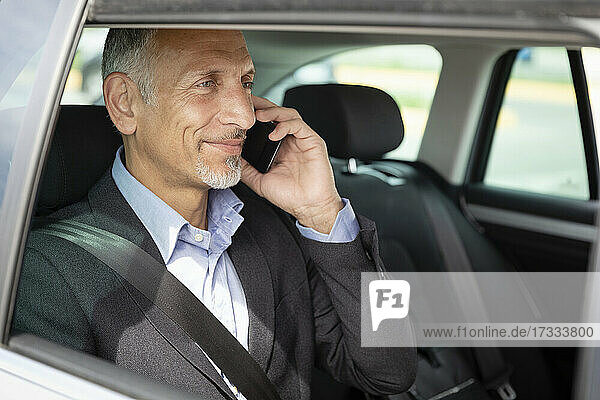 Lächelnder männlicher Berufstätiger  der im Auto mit einem Mobiltelefon spricht