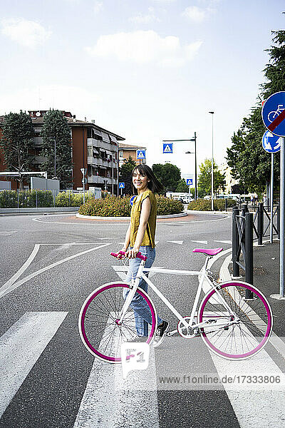 Smiling woman with bicycle standing on road