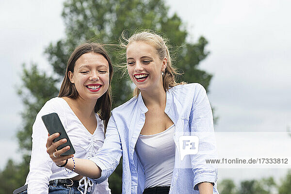 Young woman taking selfie through mobile phone with female friend