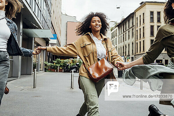 Lächelnde Frau hält die Hände ihrer Freunde beim Laufen auf der Straße