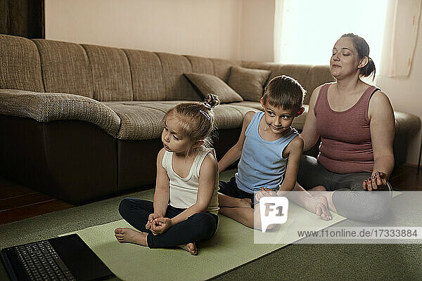 Mutter macht Yoga mit ihrem Sohn und ihrer Tochter  während sie sich ein Online-Tutorial auf dem Laptop ansieht
