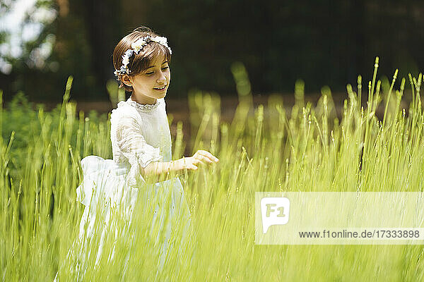 Mädchen im weißen Kleid berührt am Tag ihrer Kommunion das Gras