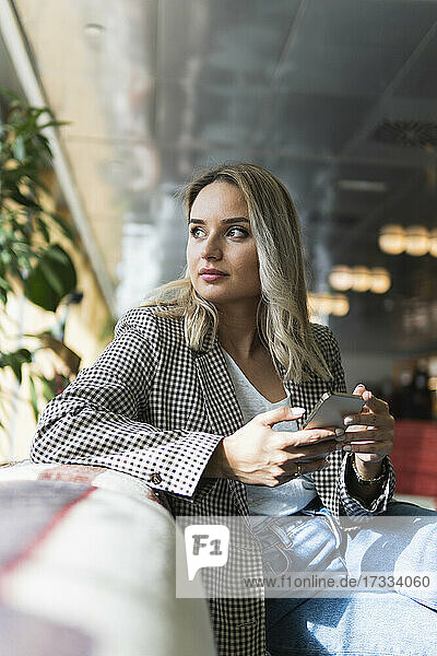 Geschäftsfrau mit Mobiltelefon  die in einem Café sitzt und nachdenkt